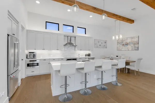 a large kitchen with white cabinets a sink dishwasher a stove a dining table and chairs with wooden floor