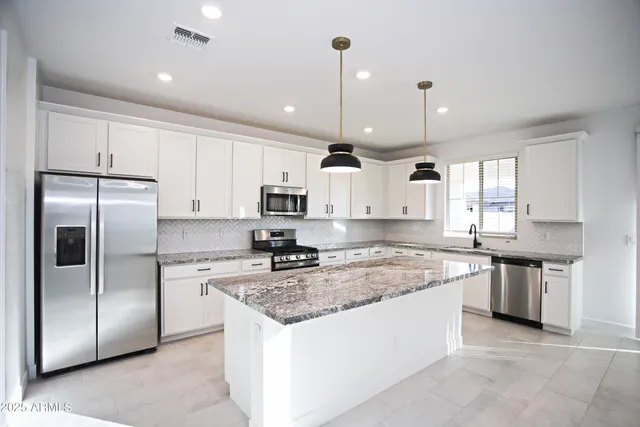 a large kitchen with stainless steel appliances granite countertop a stove top oven a sink and a refrigerator