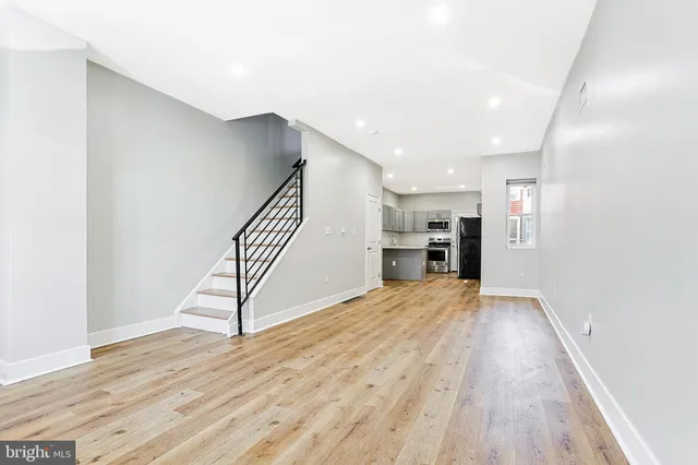 a view of empty room with wooden floor and kitchen