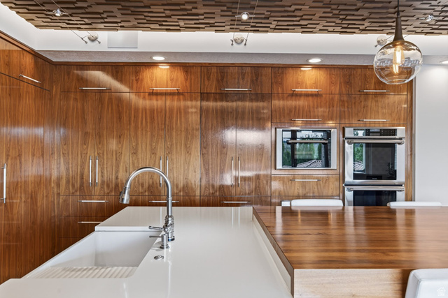 12308 Mariah Circle Draper, UT 84020 - Photo 42 of 293 Integrated kitchen featuring high-gloss walnut wood cabinetry with stainless steel hardware, a white undermount sink with a gooseneck faucet, and a light wood-finish island countertop