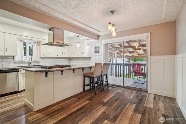 a kitchen with stainless steel appliances granite countertop a stove top oven a sink dishwasher white cabinets with wooden floor and chairs