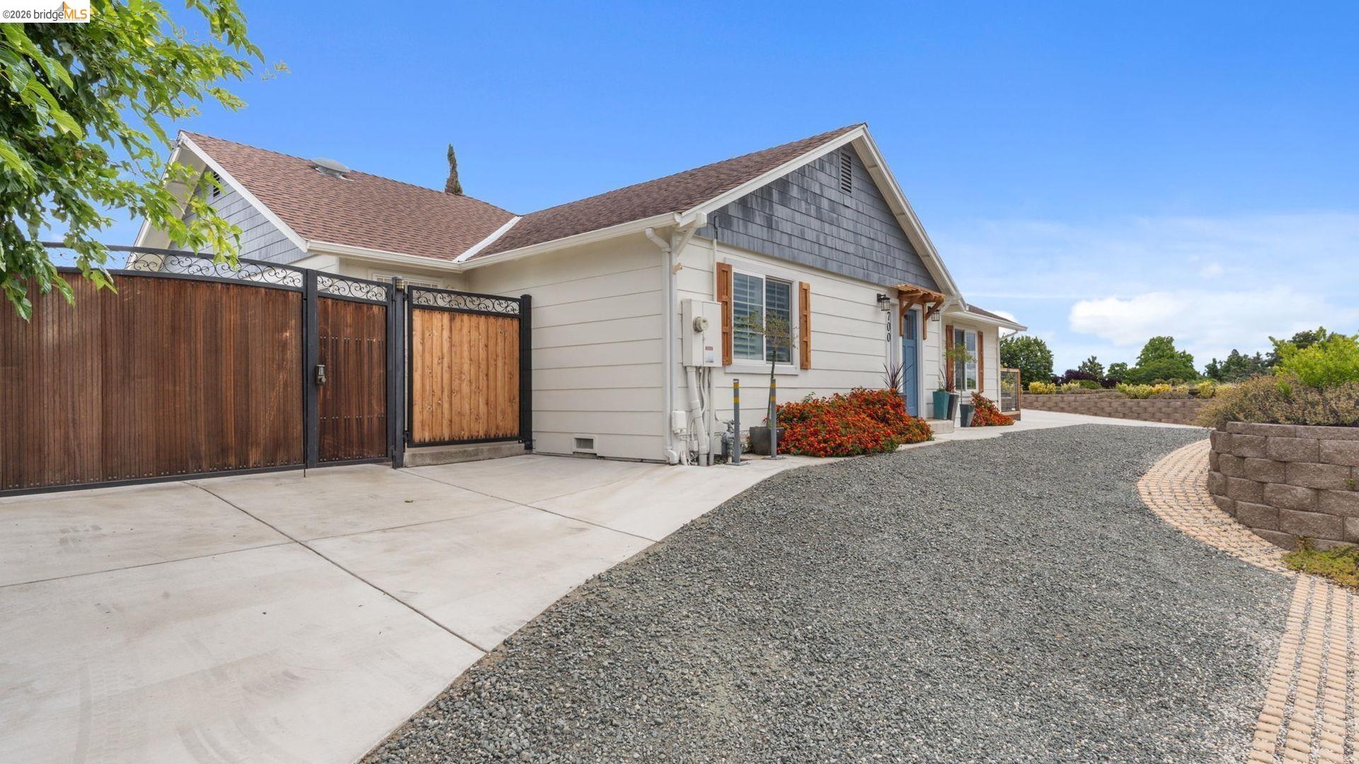 700 Brownstone Road Oakley, CA 94561 - Photo 56 of 58 Wood panel and wrought iron gates, gravel driveway, concrete pad, horizontal siding exterior, and a stone retaining wall