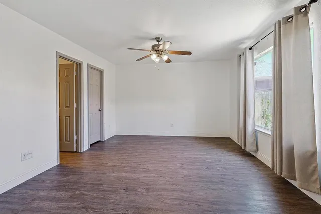 an empty room with wooden floor fan and windows