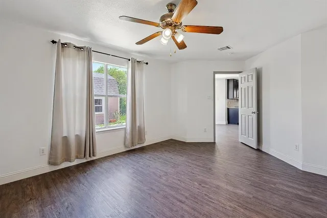 an empty room with wooden floor chandelier fan and windows