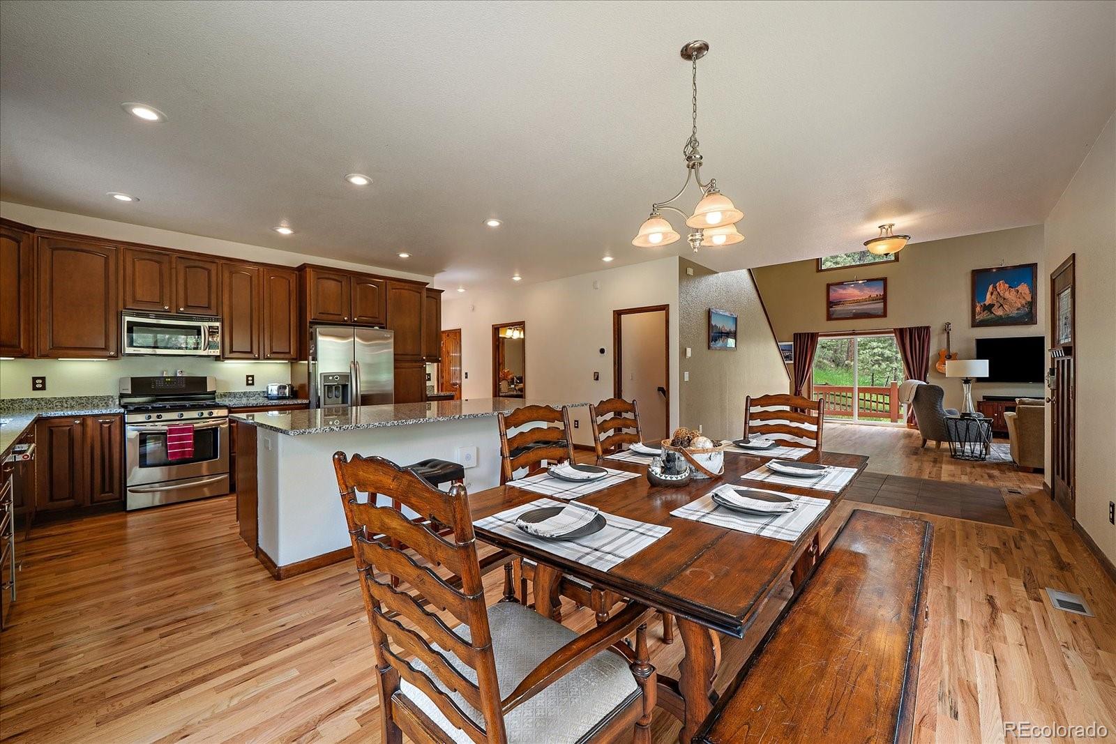 27756 Troublesome Gulch Road Evergreen, CO 80439 - Photo 15 of 47 a kitchen with stainless steel appliances kitchen island granite countertop a stove top oven a sink a dining table and chairs with wooden floor