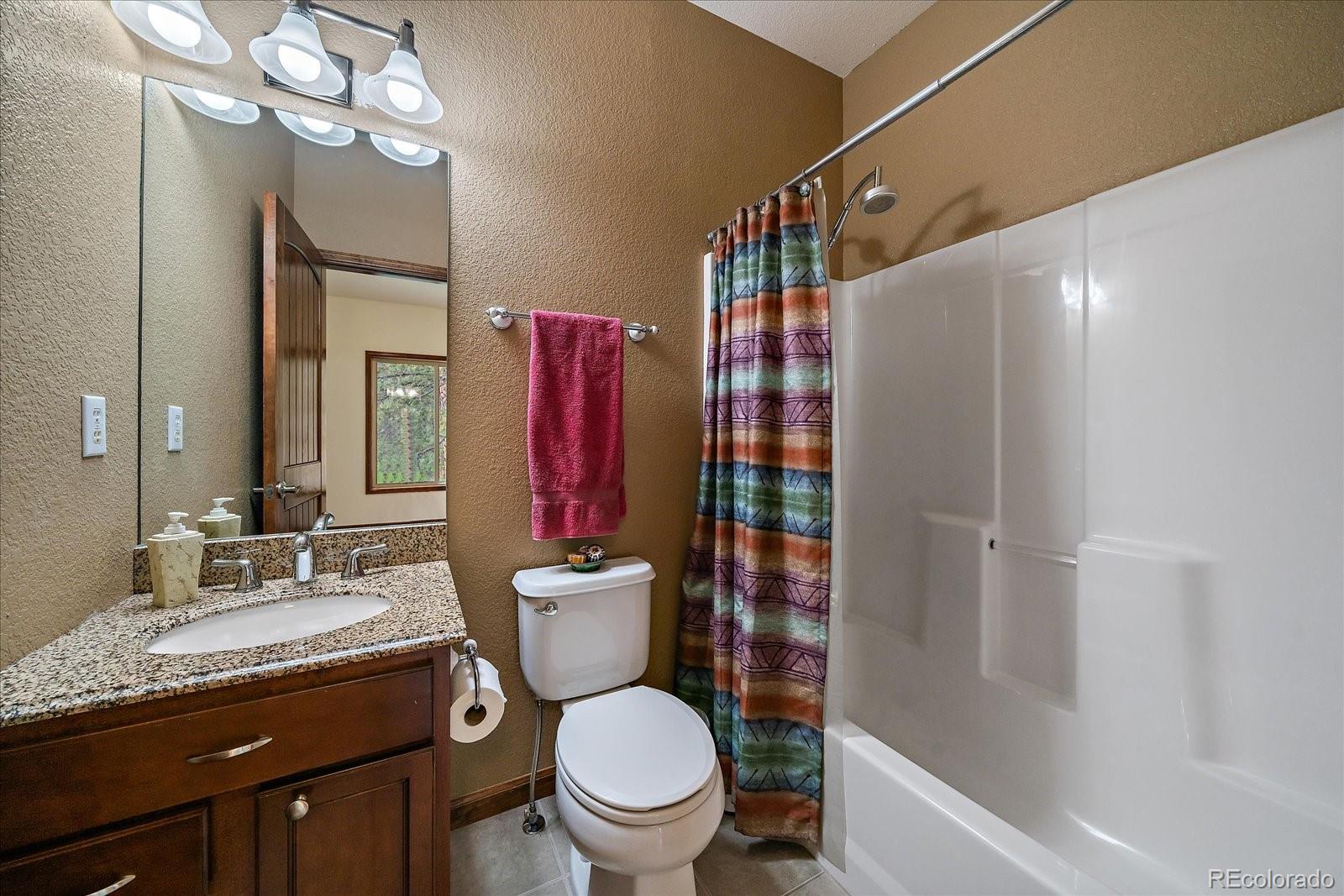 27756 Troublesome Gulch Road Evergreen, CO 80439 - Photo 31 of 47 a bathroom with a granite countertop toilet sink and mirror