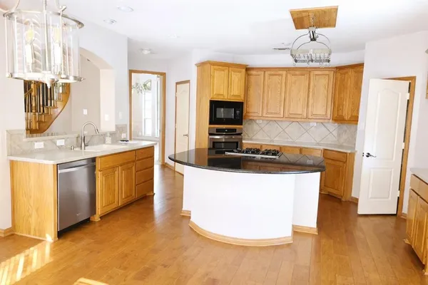 a kitchen with stainless steel appliances a sink a stove a refrigerator a microwave a dining table and chairs with wooden floor