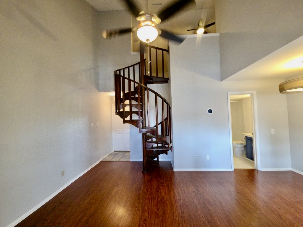 2500 Burleson Road, Unit 521 Austin, TX 78741 - Photo 5 of 20 Living area featuring a prominent dark wood spiral staircase, high vaulted ceilings, wood-finish flooring, and multiple ceiling fans