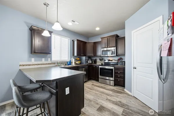 a kitchen with stainless steel appliances granite countertop a sink a stove a refrigerator cabinets and a dining table