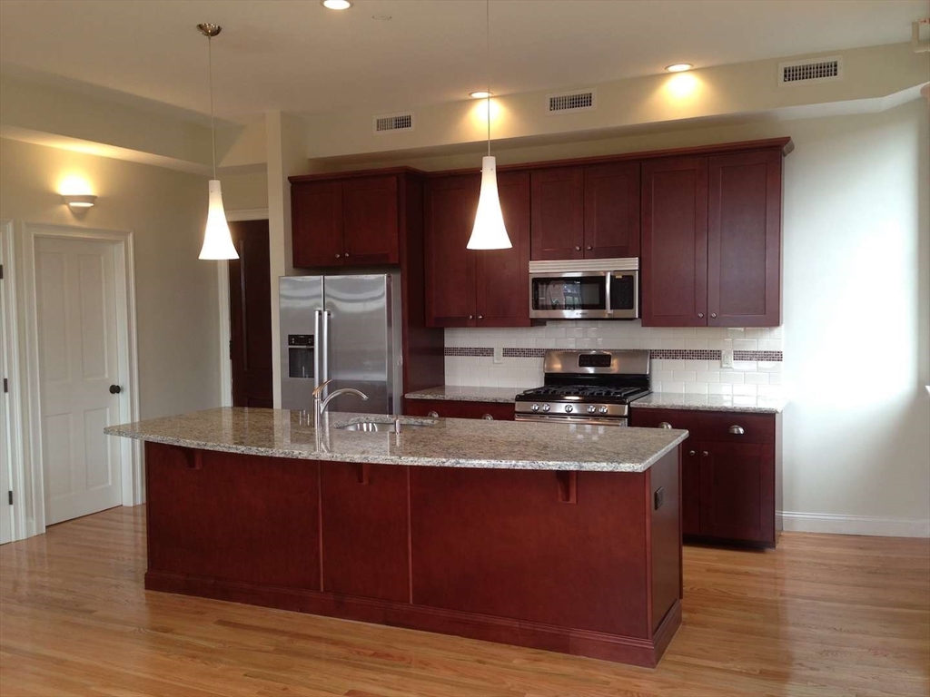 191 Main Street, Unit 2B Gloucester, MA 01930 - Photo 7 of 20 a kitchen with kitchen island granite countertop wooden cabinets and stainless steel appliances