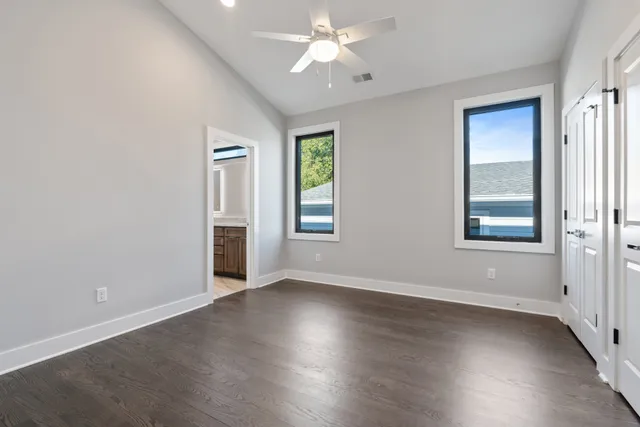 an empty room with wooden floor chandelier fan and windows