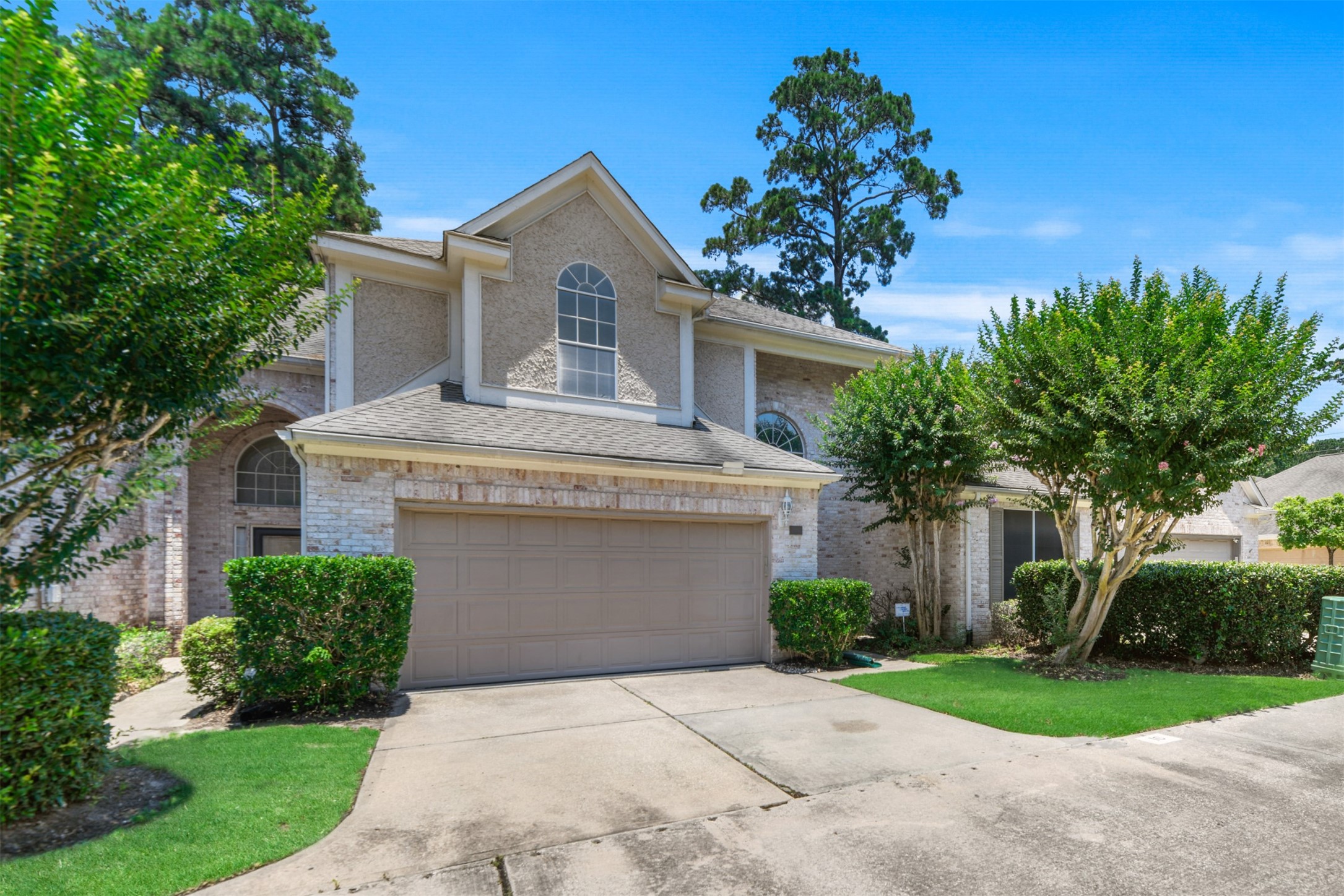 14420 Walters Road, Unit 16 Houston, TX 77014 - Photo 2 of 27 This is a charming two-story brick home with a gable roof, featuring a spacious two-car garage. The property is surrounded by well-maintained greenery, including shrubs and mature trees, offering a welcoming and serene curb appeal.