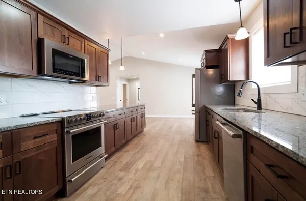 a kitchen with stainless steel appliances granite countertop a sink a stove top oven and wooden floors