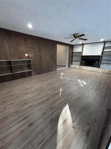 an empty room with wooden floor kitchen view and windows