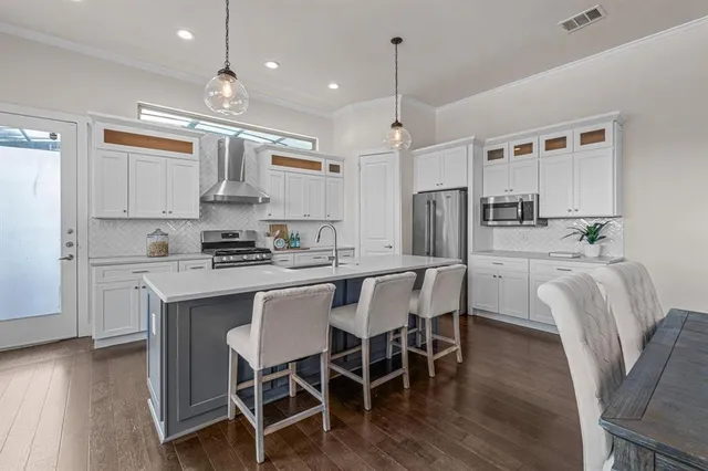 a kitchen with stainless steel appliances granite countertop a stove a refrigerator a kitchen island a dining table and chairs with wooden floor