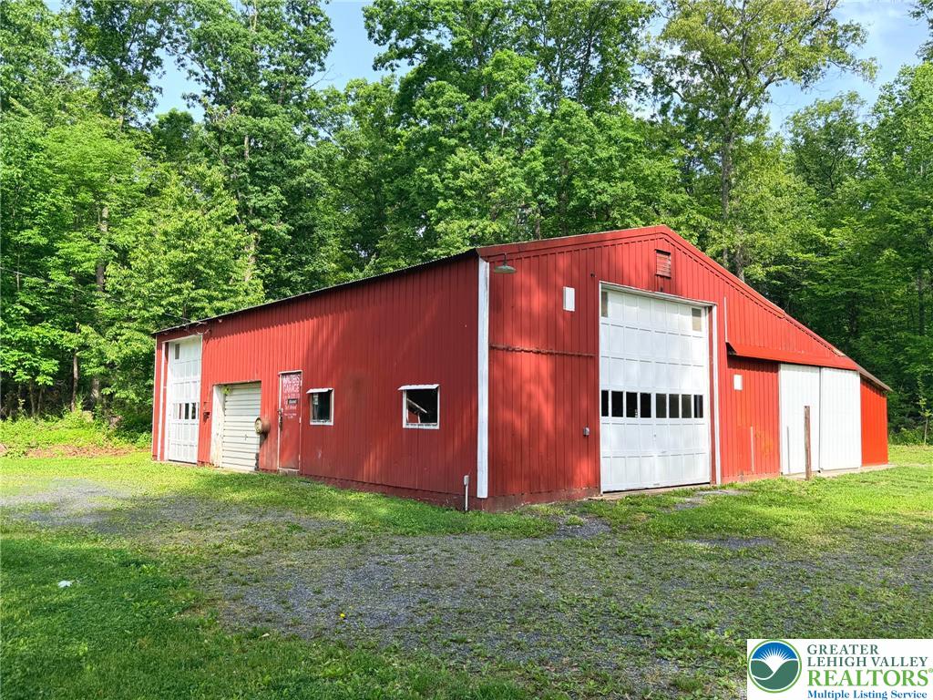 4995 Mountain Road Slatington, PA 18080 - Photo 23 of 30 A spacious red barn with multiple bay doors offers ample storage and workspace, set against a backdrop of mature trees.