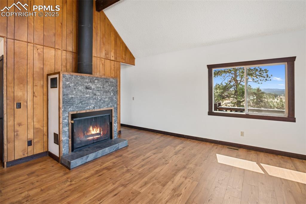 39609 Highway 24 Lake George, CO 80827 - Photo 9 of 46 Unfurnished living room with lofted ceiling with beams, baseboards, wood finished floors, stone on the fireplace