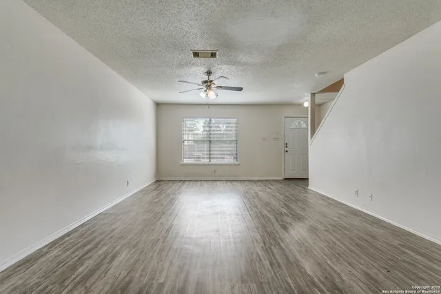 an empty room with wooden floor chandelier fan and windows