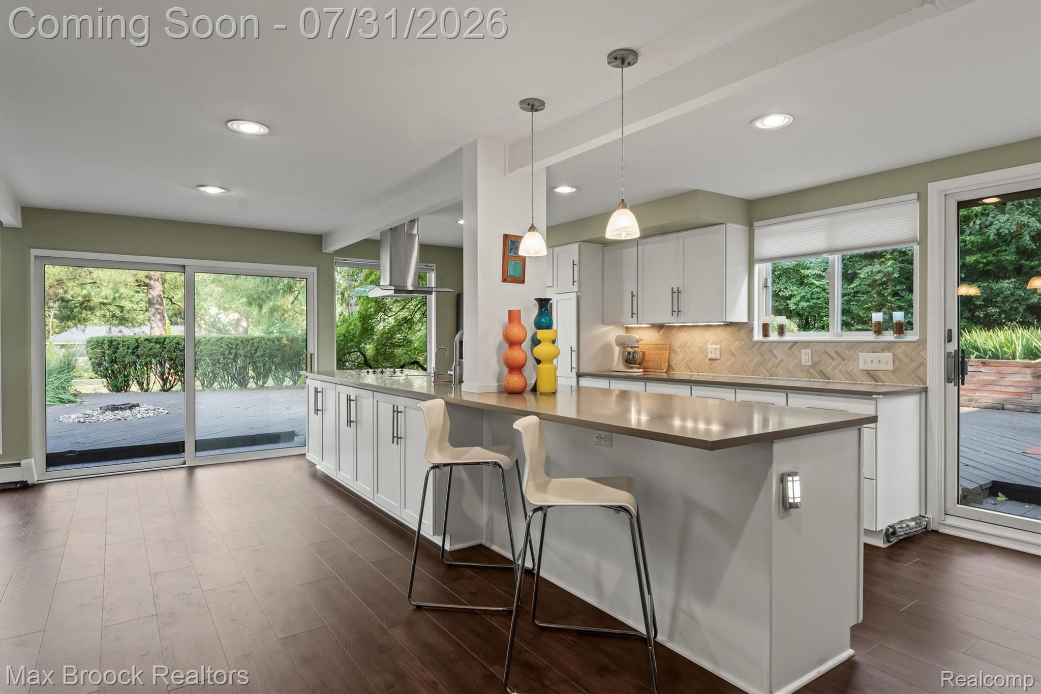 Modern kitchen featuring a breakfast bar with pendant lighting, white cabinetry, a herringbone tile backsplash, and LVF flooring