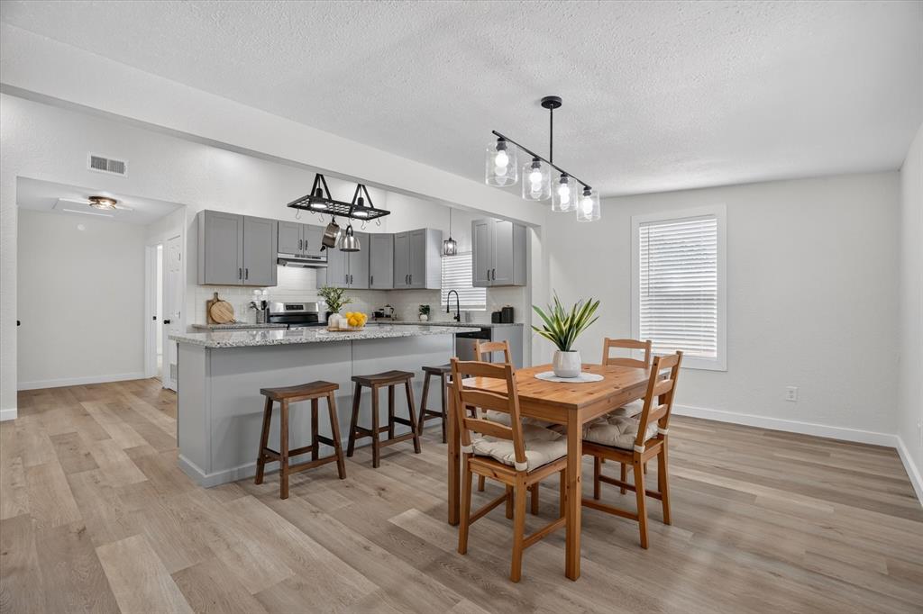 795 Meadow Road Springtown, TX 76082 - Photo 5 of 25 Open-concept living area featuring wood-finish flooring, a kitchen island with seating, grey cabinetry, stainless steel appliances, and a modern dining light fixture