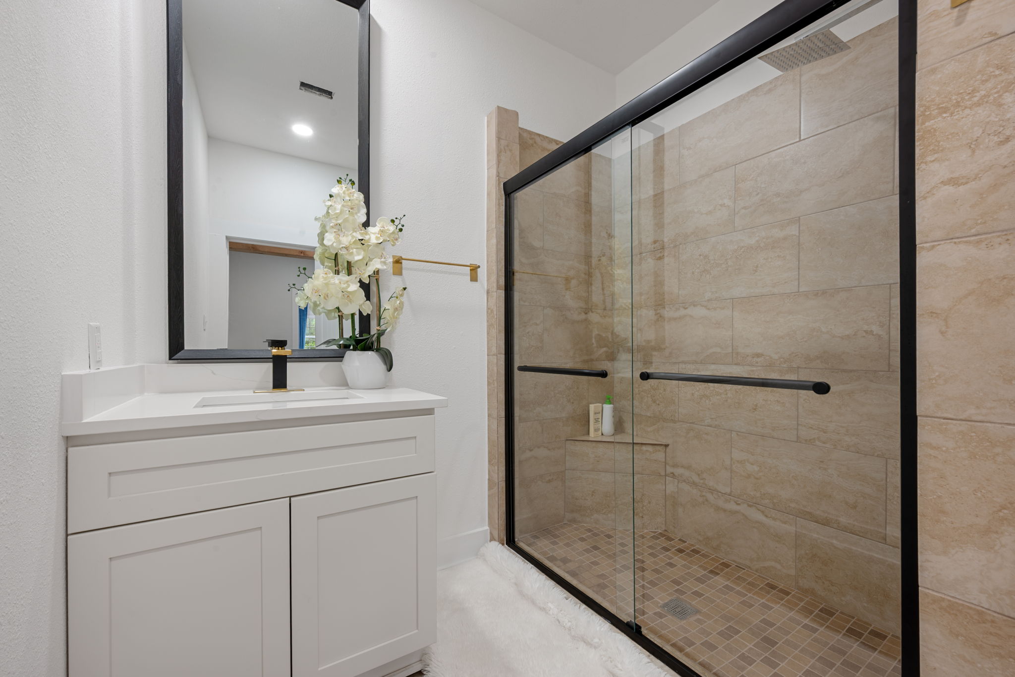 602 East 6th Street Cameron, TX 76520 - Photo 24 of 40 Bathroom featuring a vanity with a white countertop and rectangular sink, black-framed mirror, glass-enclosed shower with tiled walls, and a recessed shower shelf