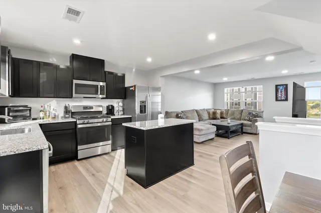 a large white kitchen with stainless steel appliances kitchen island granite countertop a stove top oven a sink dishwasher a dining table and chairs with wooden floor