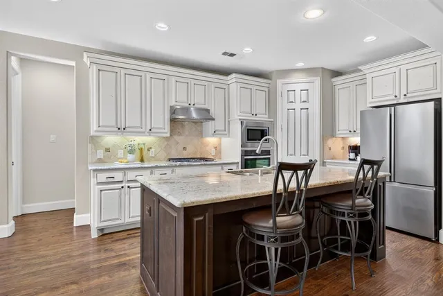 a kitchen with a refrigerator a stove a sink and white cabinets with wooden floor