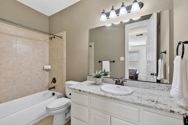 a bathroom with a granite countertop sink a toilet a mirror a bathtub and shower