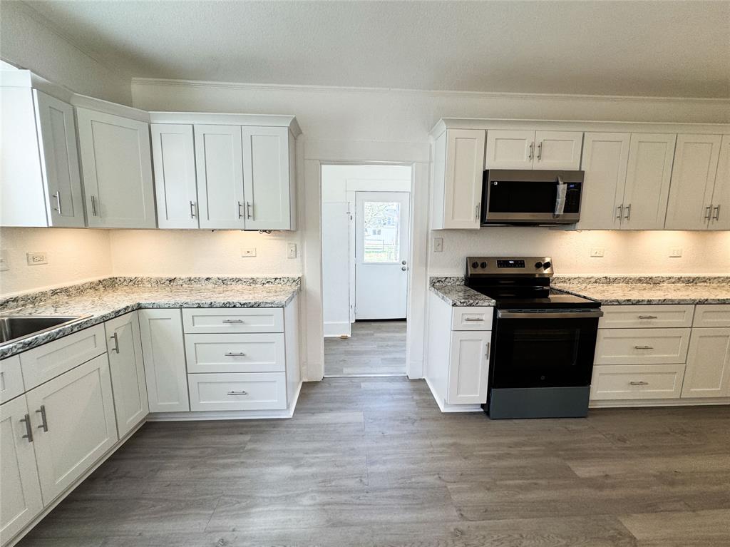 904 West 7th Street Cisco, TX 76437 - Photo 17 of 37 a kitchen with granite countertop white cabinets and stainless steel appliances