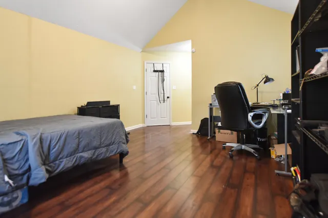a bedroom with a bed a desk and chair with wooden floor
