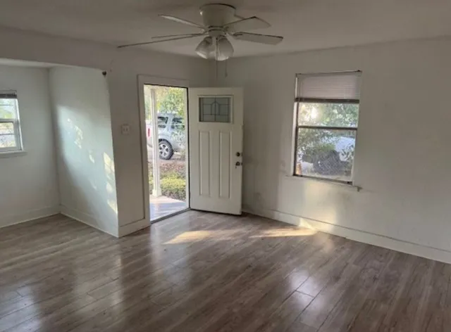 an empty room with wooden floor chandelier fan and windows