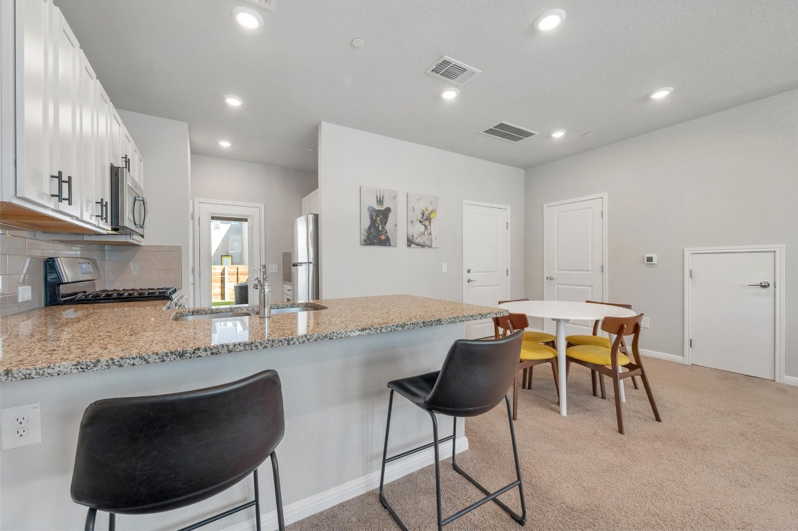 9015 Cattle Baron Path, Unit 403 Austin, TX 78747 - Photo 10 of 40 a kitchen with stainless steel appliances granite countertop a stove a sink a dining table and chairs