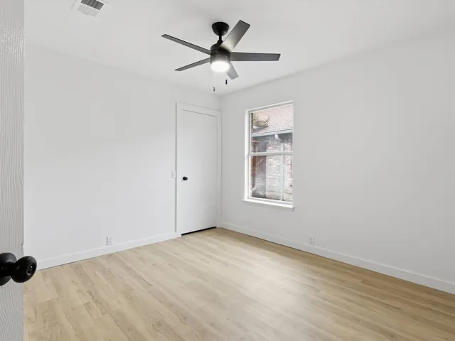 an empty room with wooden floor chandelier fan and windows