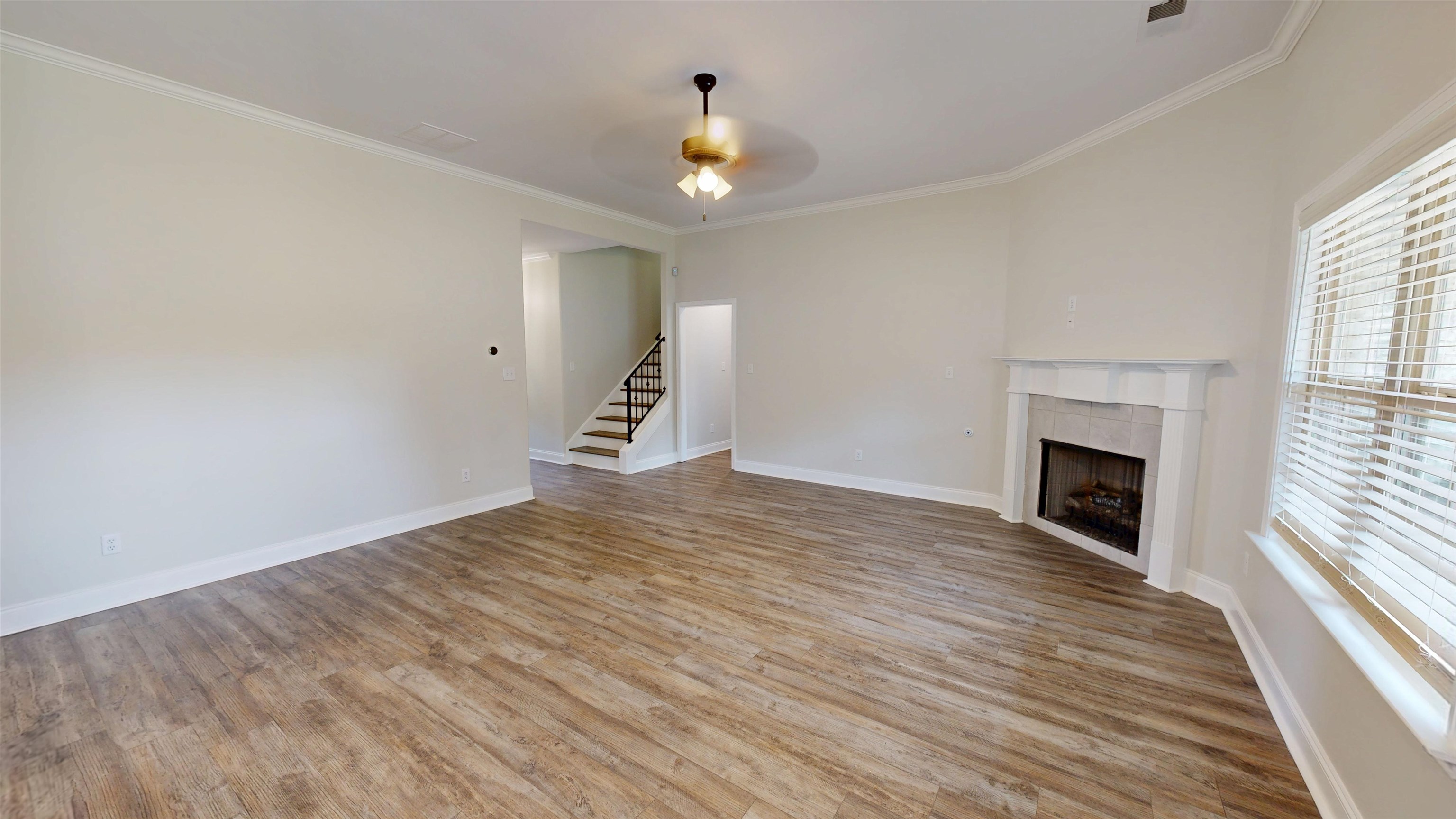 Unfurnished living room with ornamental molding, light wood-type flooring, a tile fireplace, stairway, and a ceiling fan