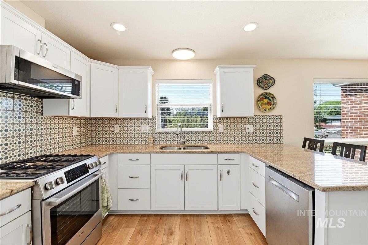 6710 West Ustick Road Boise, ID 83704 - Photo 11 of 42 Contemporary kitchen featuring white cabinetry, stainless steel appliances, granite countertops, patterned tile backsplash, and wood-finish flooring