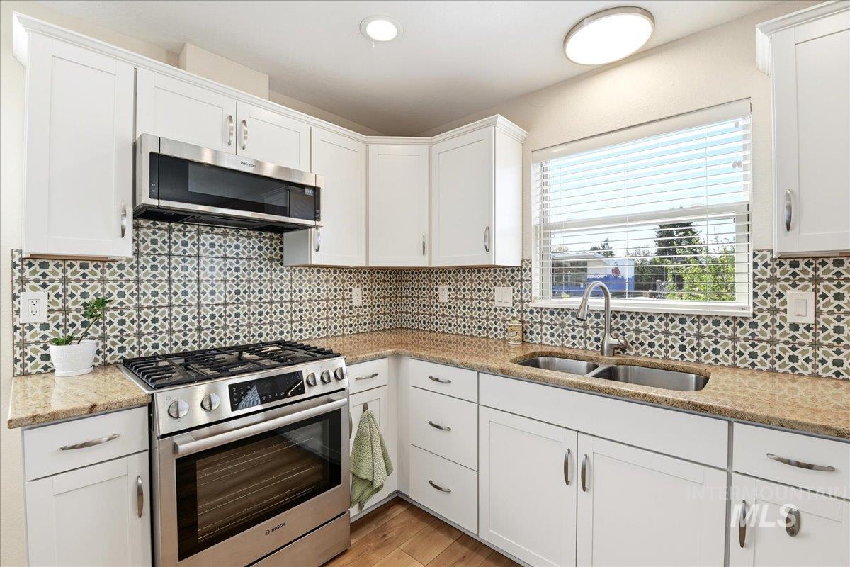 6710 West Ustick Road Boise, ID 83704 - Photo 12 of 42 Modern kitchen featuring white cabinetry, granite-finish countertops, and a patterned tile backsplash
