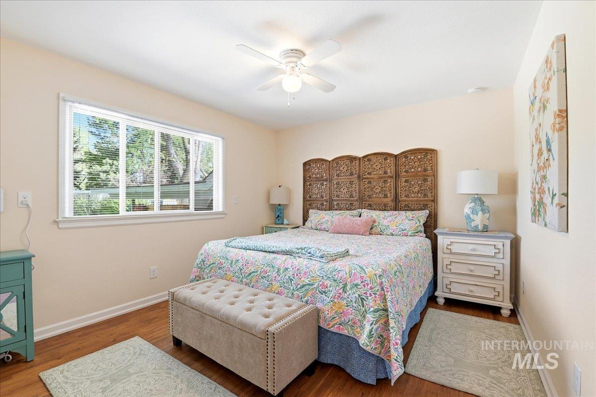 6710 West Ustick Road Boise, ID 83704 - Photo 15 of 42 Warm bedroom featuring wood-finish flooring, a multi-panel window, and a ceiling fan with integrated lighting