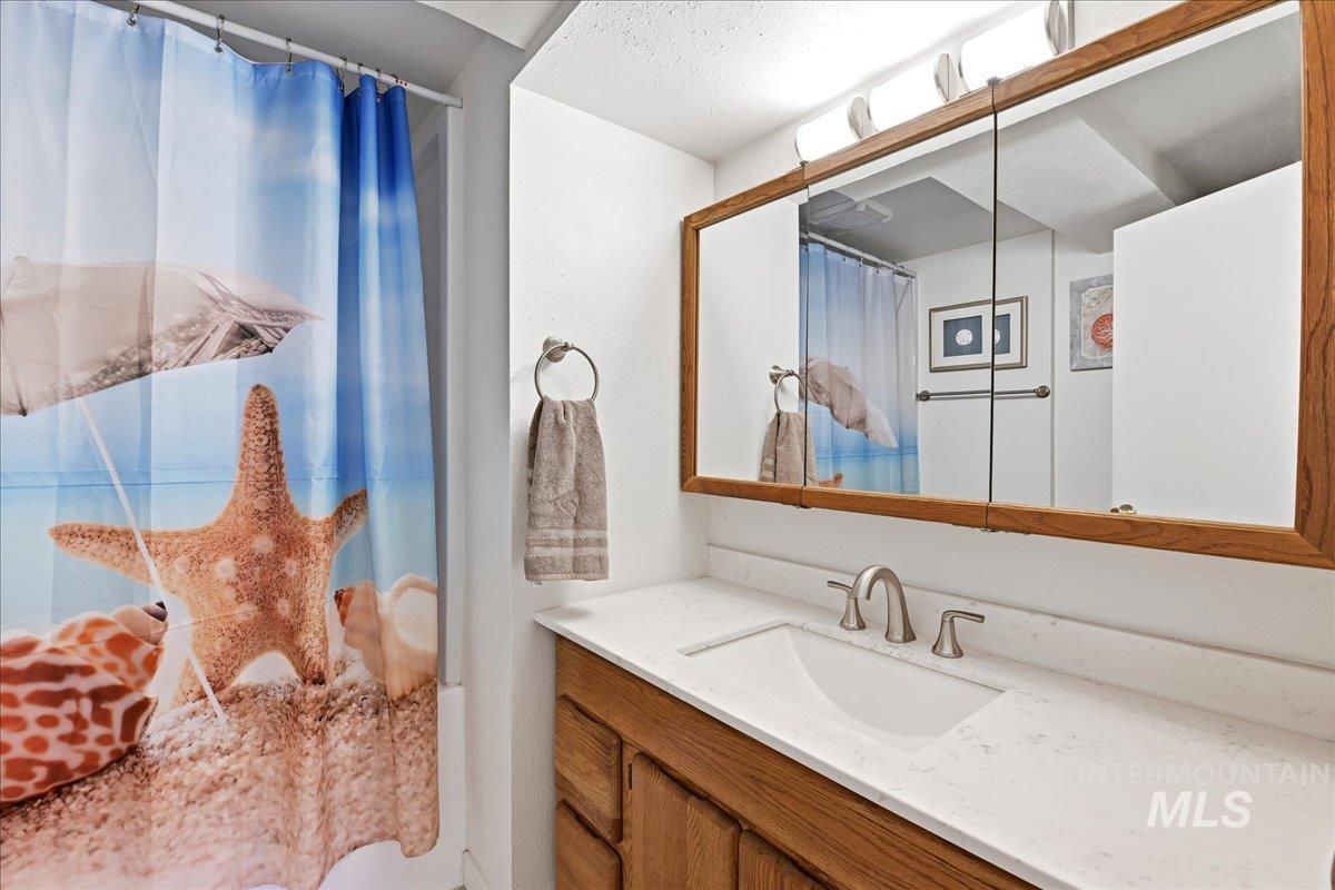 6710 West Ustick Road Boise, ID 83704 - Photo 25 of 42 Bathroom featuring a wood-framed medicine cabinet with integrated lighting, a white countertop with an undermount sink, and a brushed nickel faucet