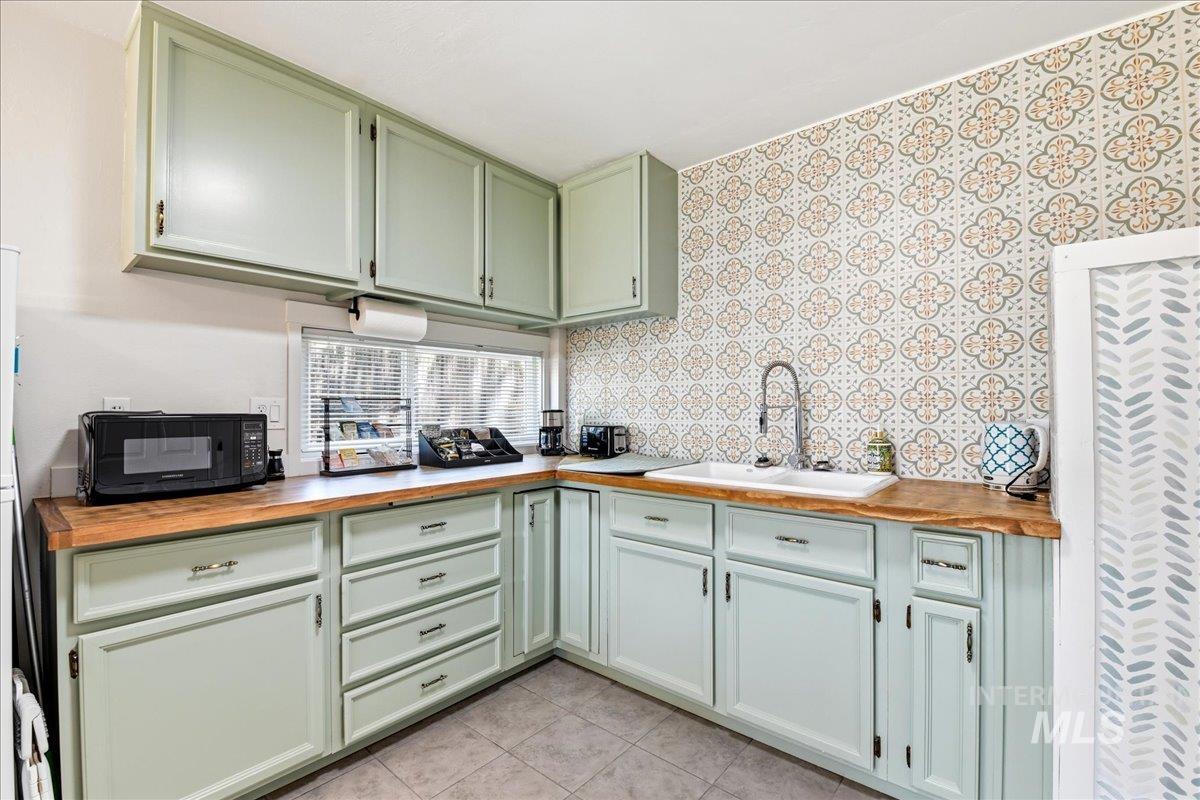 6710 West Ustick Road Boise, ID 83704 - Photo 32 of 42 Kitchen featuring light green cabinetry, wood-finish countertops, a white undermount sink with a gooseneck faucet, and patterned tile backsplash