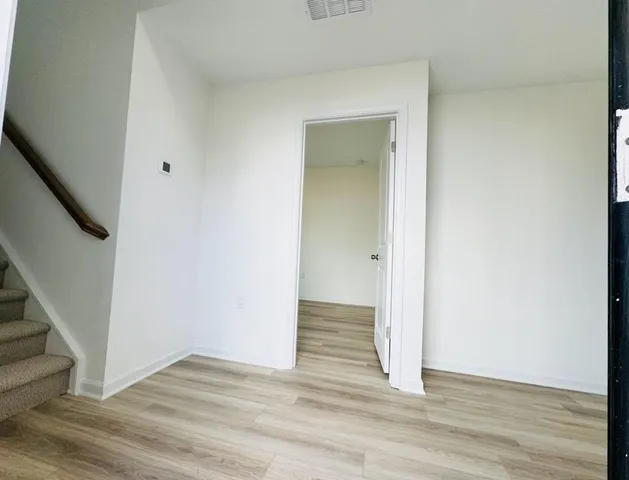 a view of an empty room with wooden floor and stairs