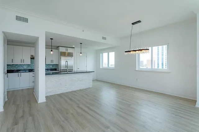 a view of an empty room with wooden floor and a kitchen