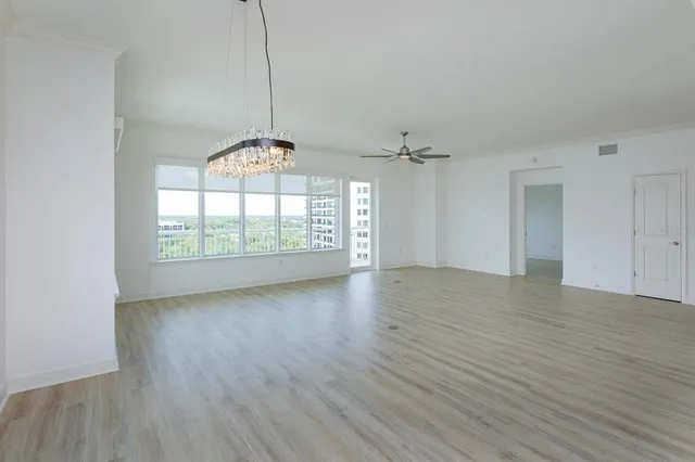 an empty room with wooden floor chandelier and windows