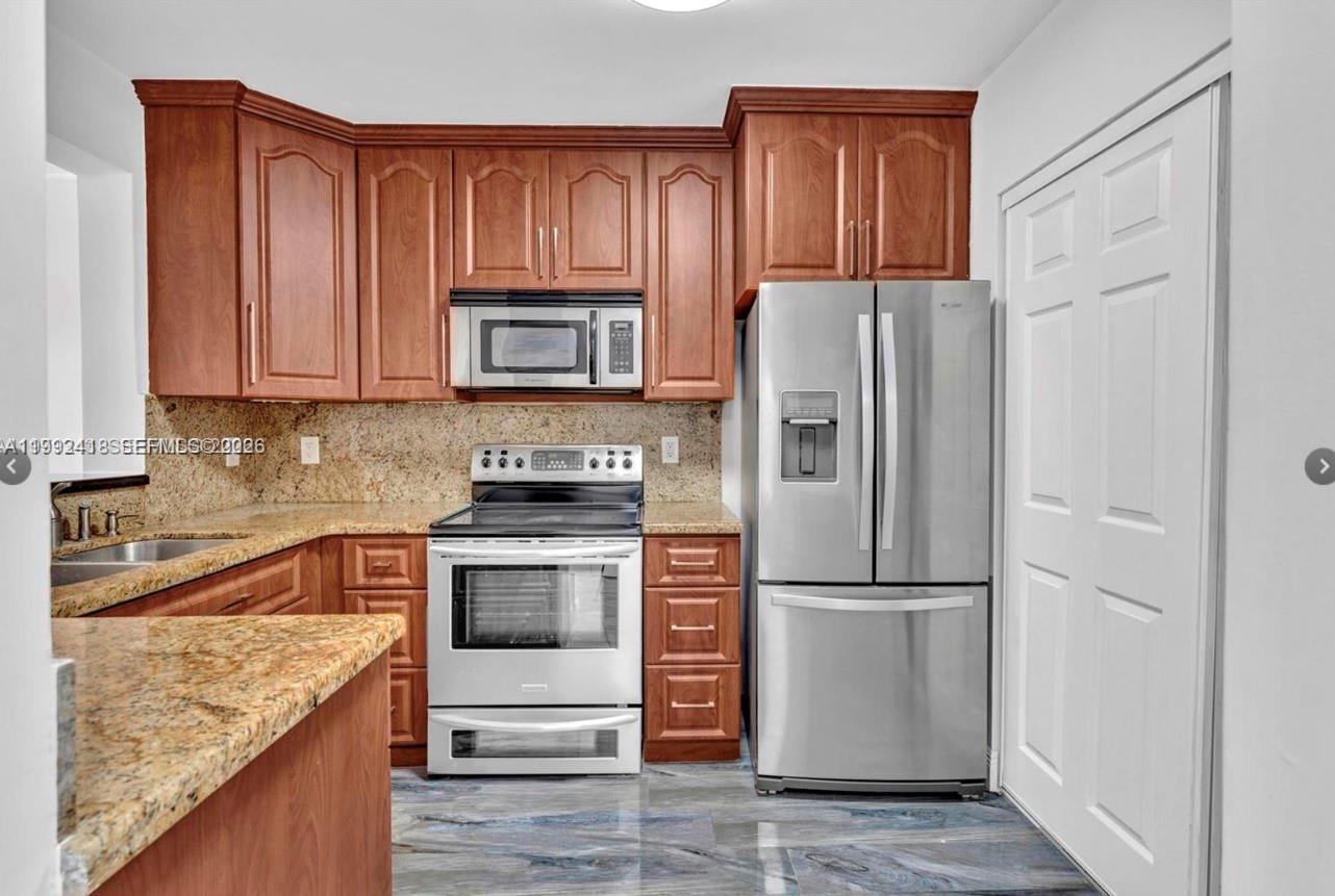 8900 Collins Avenue, Unit 304 Surfside, FL 33154 - Photo 13 of 18 a kitchen with granite countertop wooden cabinets and stainless steel appliances
