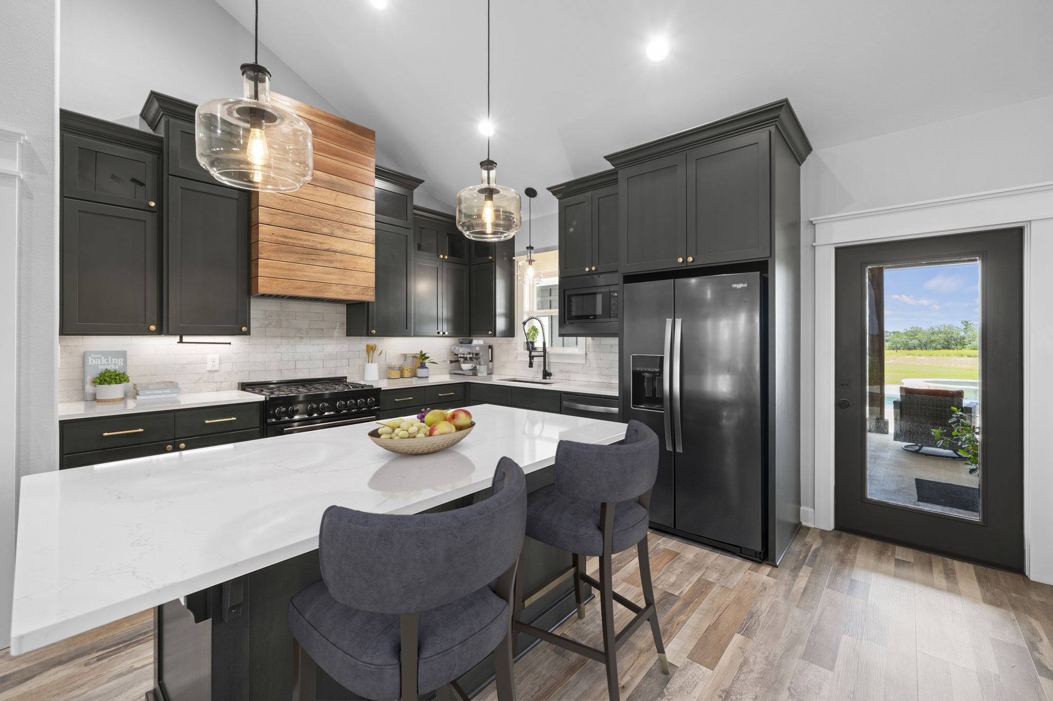 1655 Old Cuero Road Yoakum, TX 77995 - Photo 5 of 24 Virtually Staged: This stunning gourmet kitchen blends modern farmhouse charm with upscale finishes and thoughtful design. It is anchored by an oversized quartz island with bar seating, making it perfect for meal preparation, casual dining, and entertaining. Custom floor-to-ceiling black cabinetry provides abundant storage, while a striking wood-accent vent hood creates a beautiful focal point above the professional-grade gas range. Elegant pendant lighting creates a timeless feel.