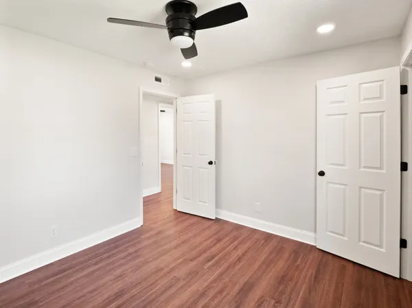 an empty room with wooden floor ceiling fan and window