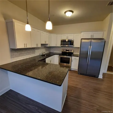 a kitchen with stainless steel appliances granite countertop a sink a stove a refrigerator a center island a stove and a wooden floors