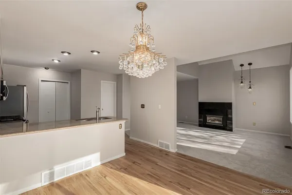 a view of an empty room with wooden floor and a kitchen