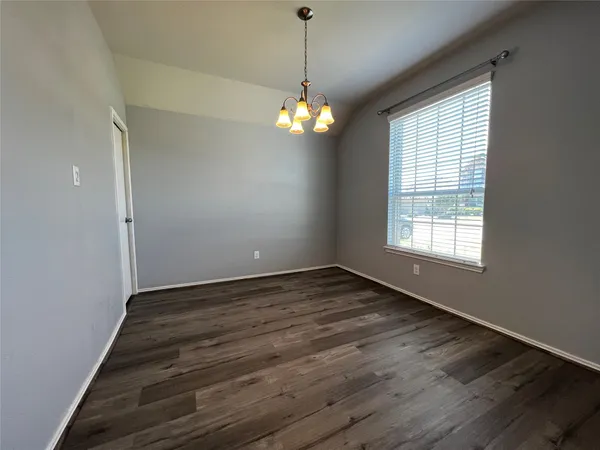 a view of an empty room with chandelier fan and wooden floor