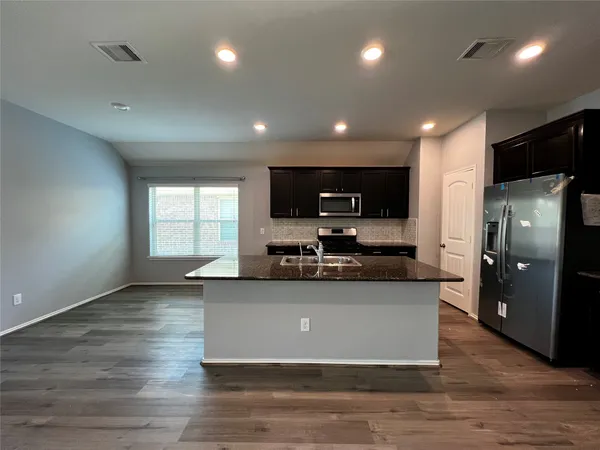 a view of a kitchen with kitchen island a sink wooden floor and stainless steel appliances