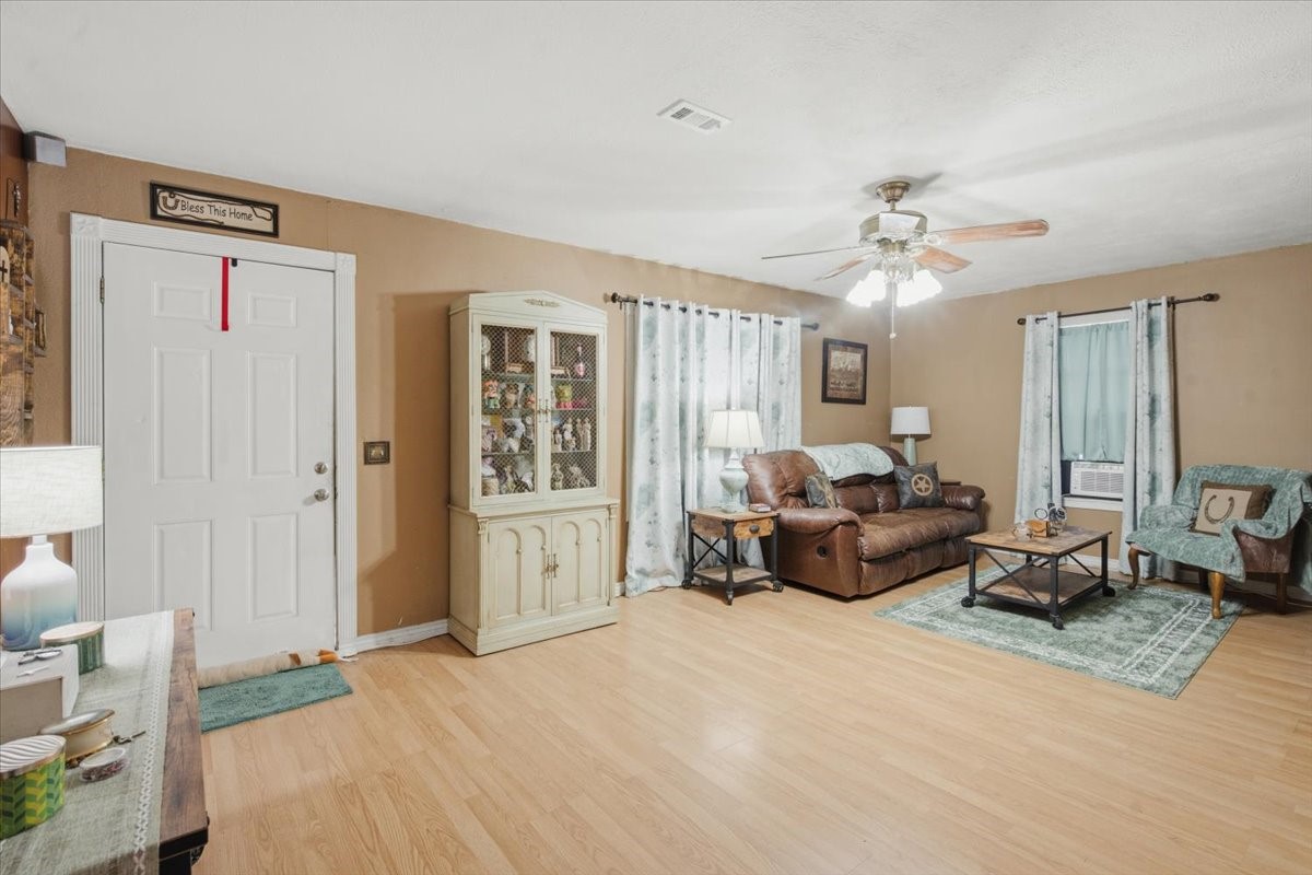 765 Norcross Road Wallis, TX 77485 - Photo 18 of 42 This spacious living room features warm-toned walls and laminate wood flooring. It includes a cozy seating area A ceiling fan provides additional comfort, Natural light filters through curtains on two windows, creating an inviting atmosphere.